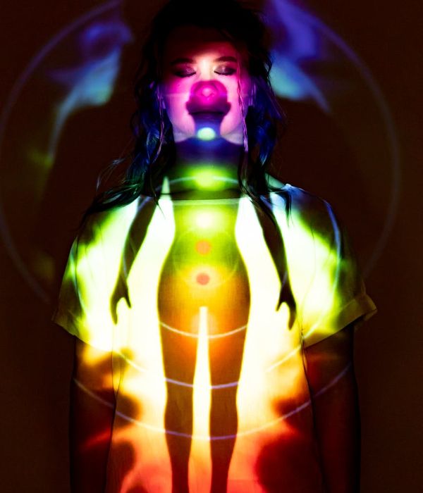 Woman in a tranquil yoga pose with a plum-colored background and aqua light.